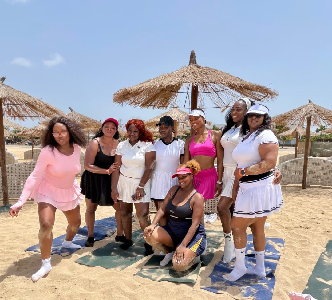 Group in tennis outfits playing beach games under thatched umbrellas
