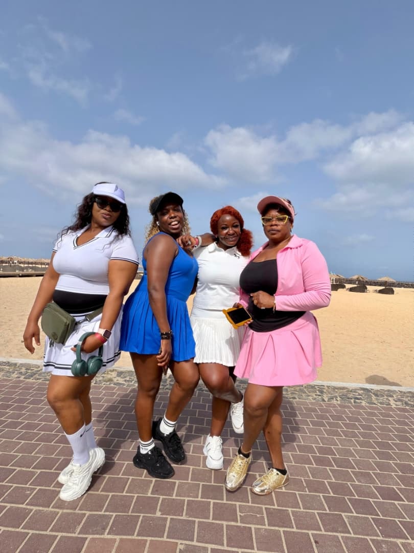 Four friends in tennis dresses posing on a beach boardwalk