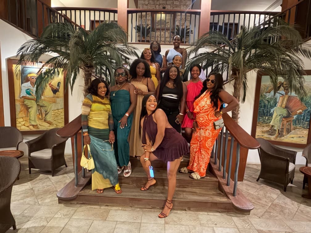 Group in colourful evening dresses posing on a resort staircase framed by palm trees