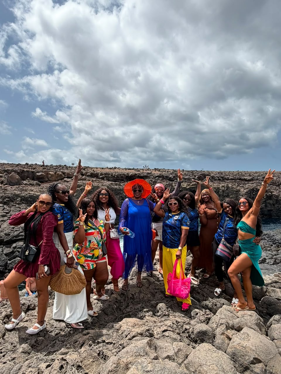 Large group cheering on volcanic rocks by the sea under a dramatic sky