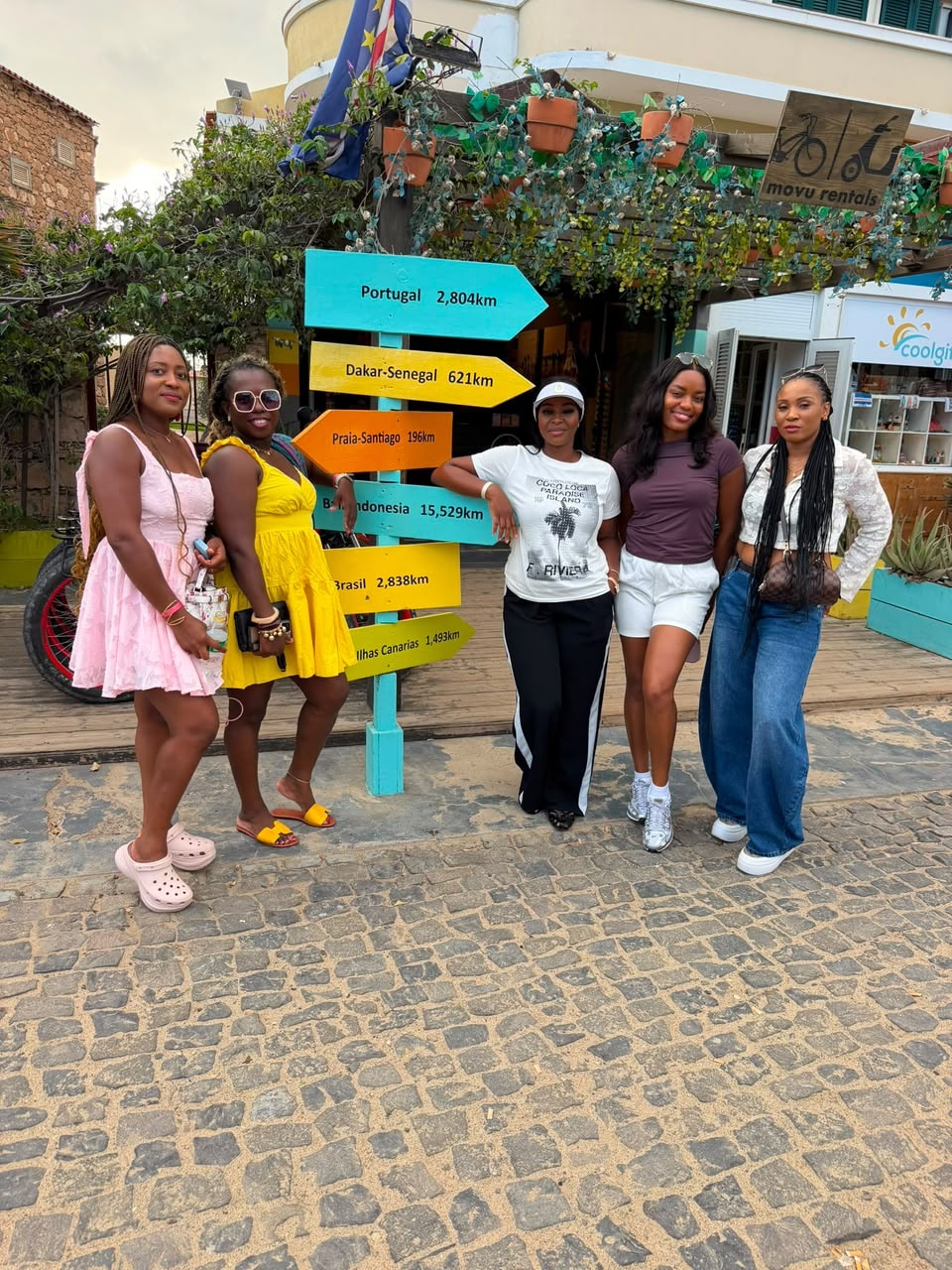 Five friends posing in front of the colourful distance signpost in Santa Maria, Cape Verde